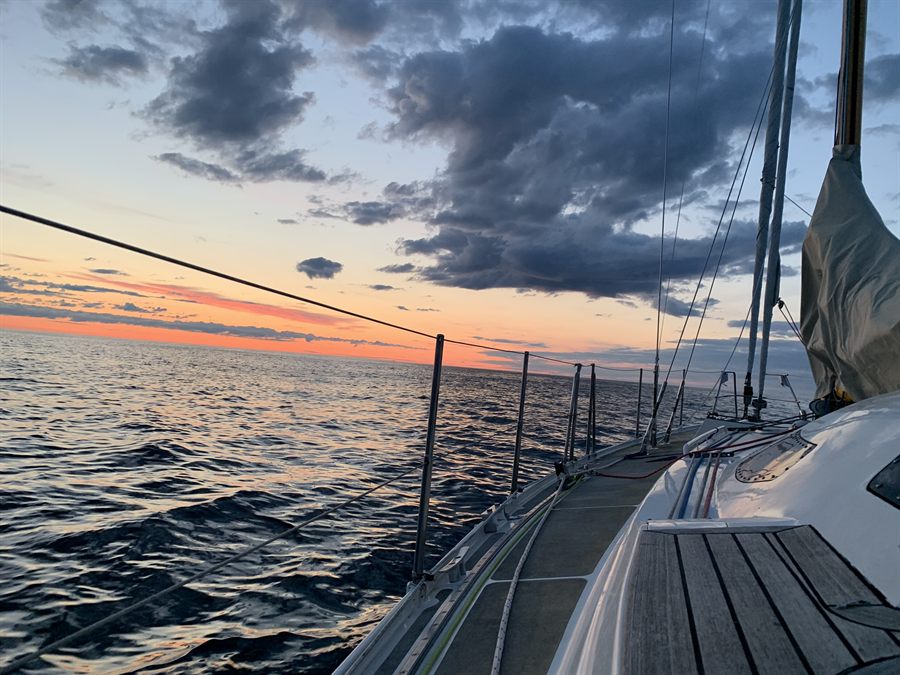 The deck and rigging of Elfri at sea, with an orange sunset along the horizon