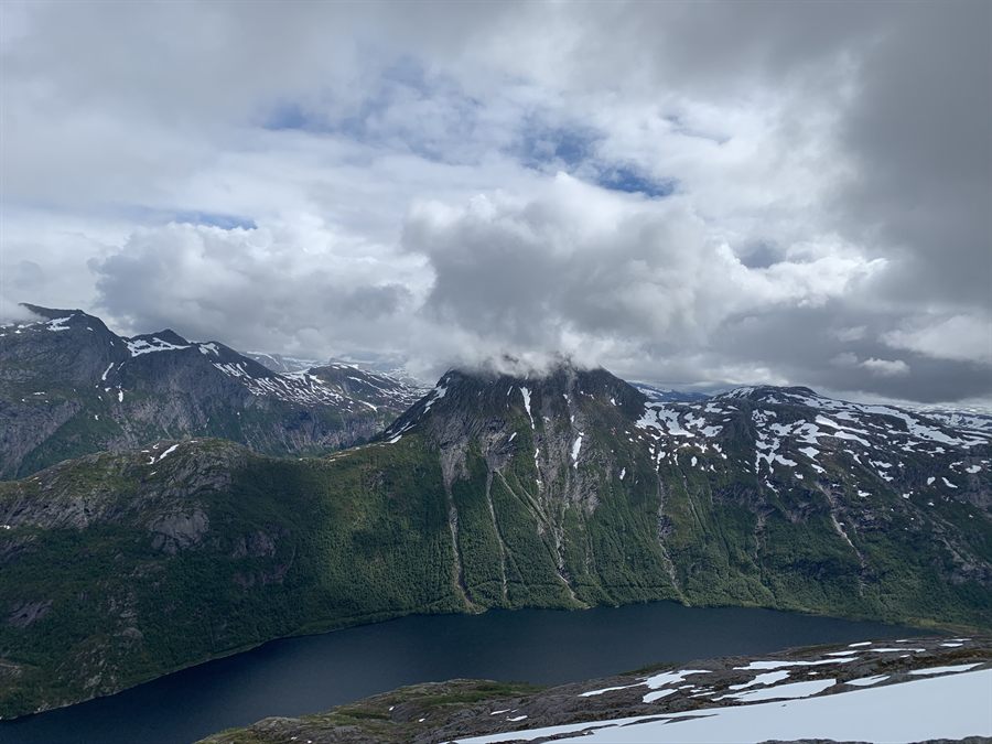 Green mountainsides with patches of snow above a dark lake, heavy cloud over the summits